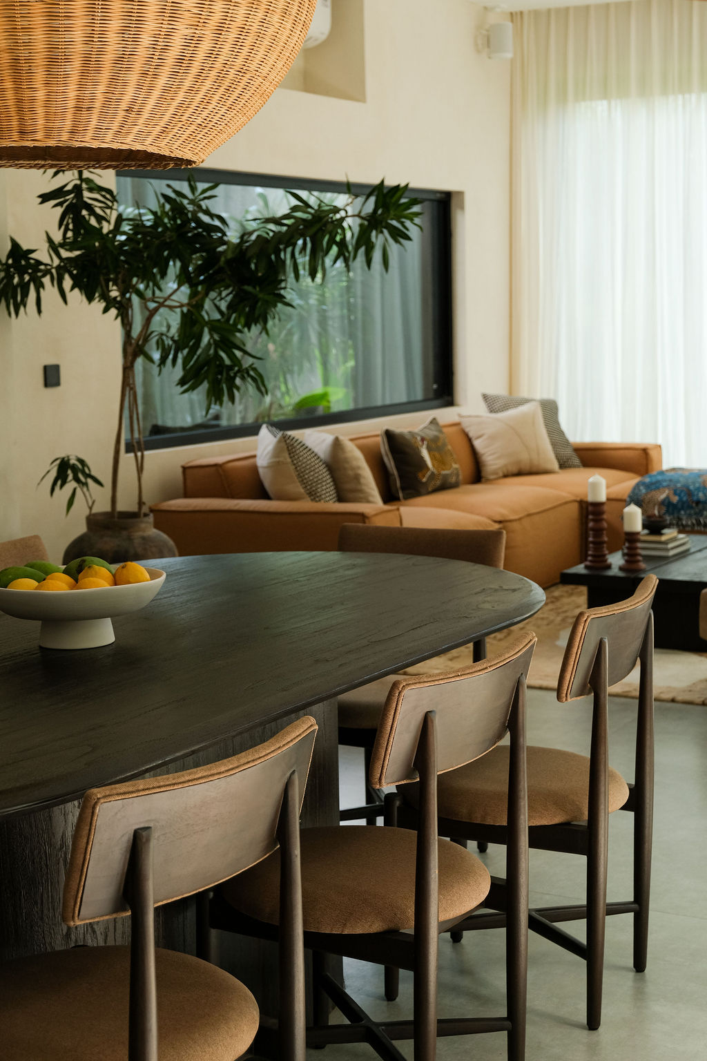 Open dining table with woven pendant light, sofa and curtains in the living area beyond