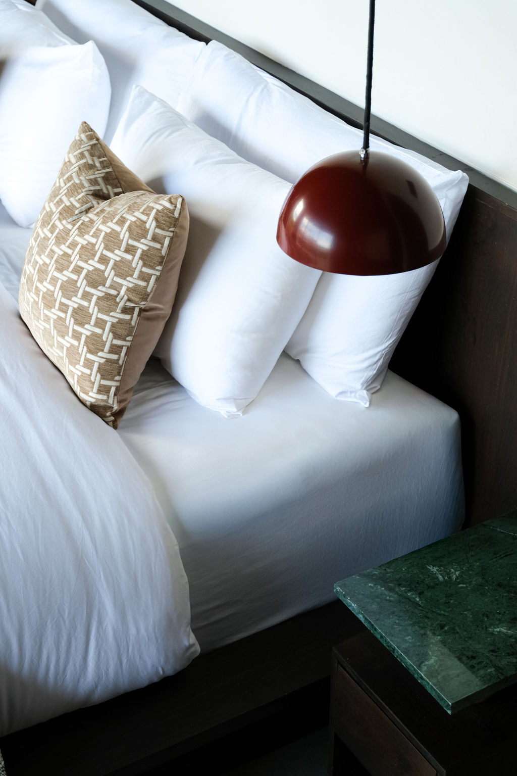 Detail of pillows and a red pendant light against white linens, with green marble nightstand