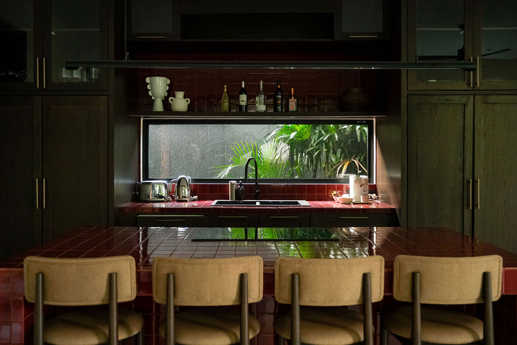 Kitchen counter in red tile with sink, garden window, and bar seating