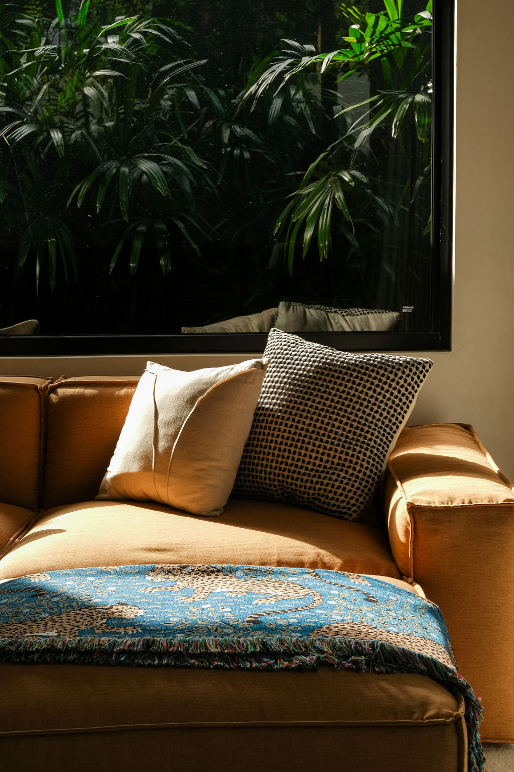 Sofa with linen and patterned cushions and a woven throw, beside a window onto the garden