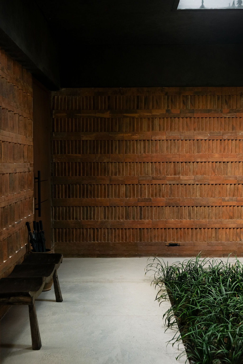 Hand-laid Balinese brick wall in the villa's foyer, with a wooden bench and tropical planting