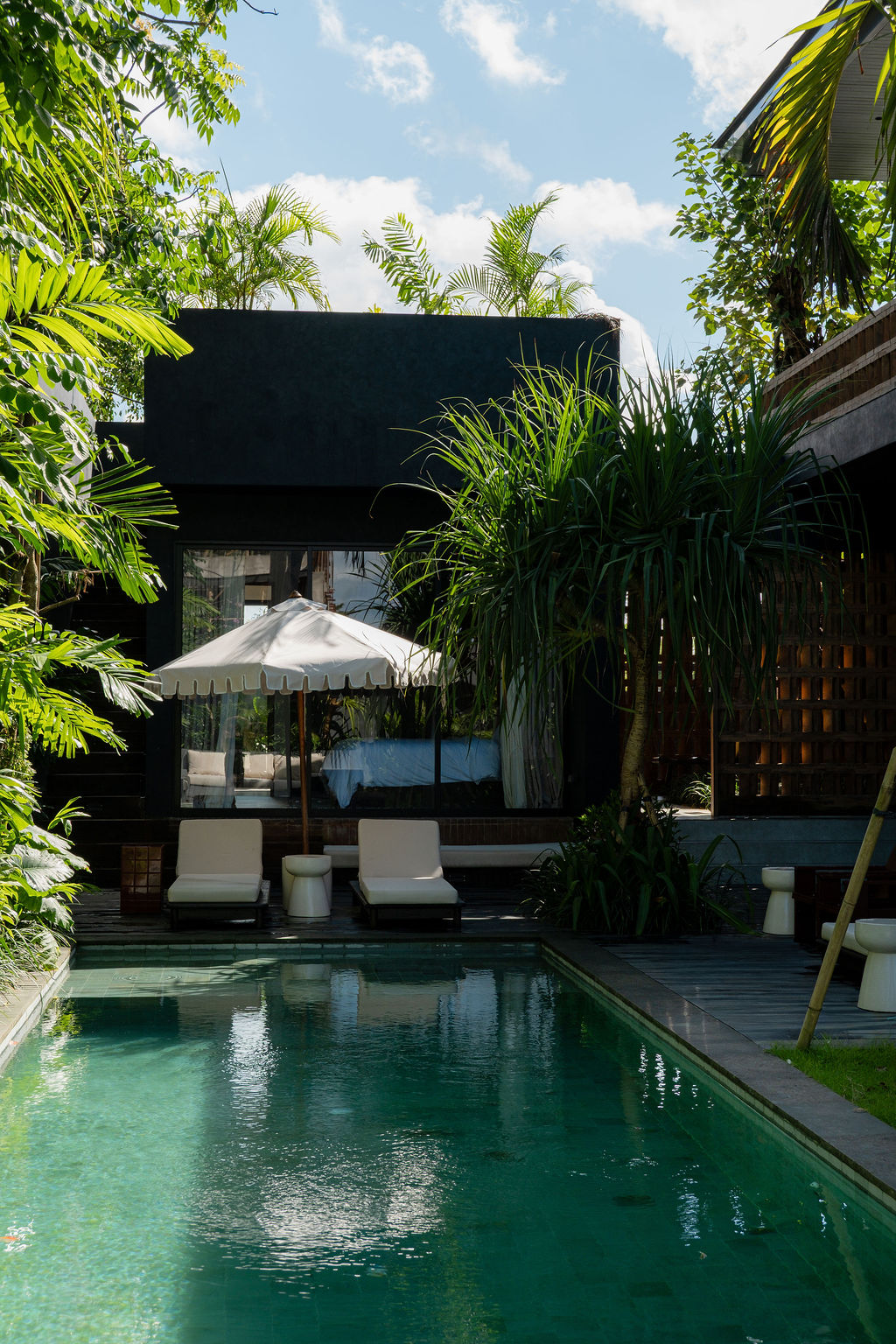 Full-length swimming pool beside the villa's dark facade, with loungers and umbrella