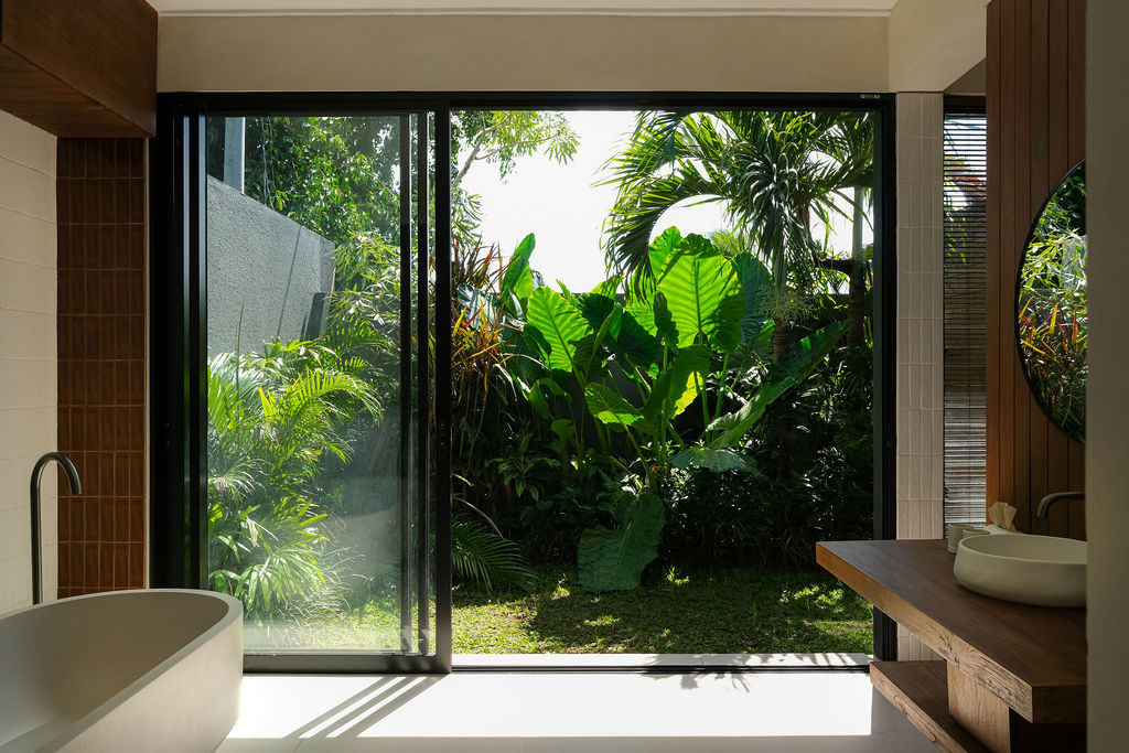 Freestanding bathtub beside a full-height glass door opening onto a garden of palms
