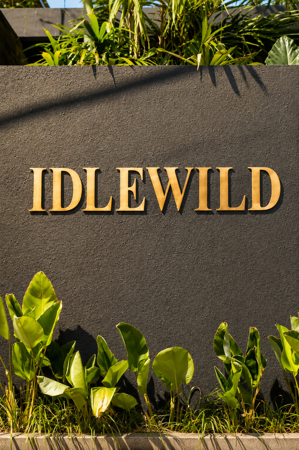 IDLEWILD signage in brass against a dark facade, framed by tropical foliage